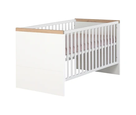 Weißes Babybett mit hellen Holzleisten oben. Eine Seite ist geschlossen, die andere hat vertikale Gitterstäbe. Ein hellrosa Spannbetttuch ist sichtbar.