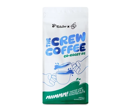 Weiße Kaffeepackung mit blauem und grünem Aufdruck, die 55 Degrees x roasted. - The Crew Coffee Co-Roast #5 Espresso - 1 kg Ganze Bohne zeigt. Oben sind die Logos von Tchibo und 55 Degrees zu sehen, darunter der Schriftzug „THE CREW COFFEE CO-ROAST #5“. Eine Illustration zeigt zwei Hände, die Kaffeetassen halten, aus denen blaue Flüssigkeit spritzt. Der untere grüne Bereich trägt die Aufschrift „MHMMM! TASTES LIKE CHOCOLATE & ROASTED NUTS“ und „1000g GANZE BOHNE“.