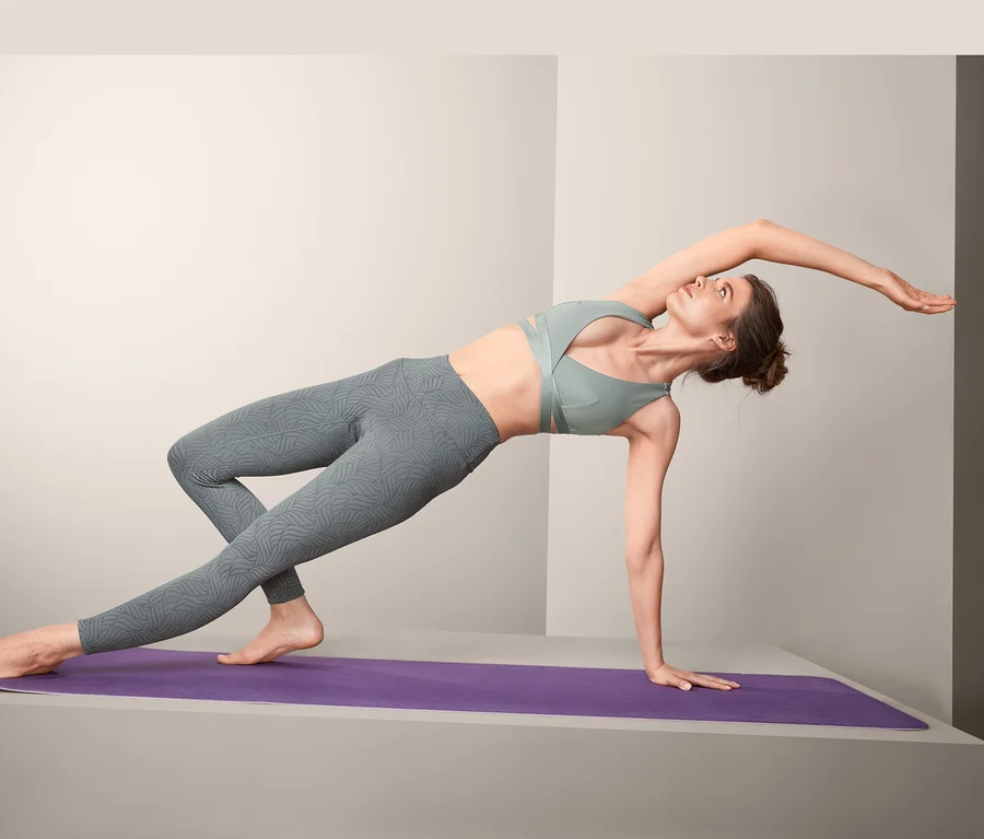 Frau macht Yogaübung auf lila Matte und trägt eine Bodyforming-Sporttight.
