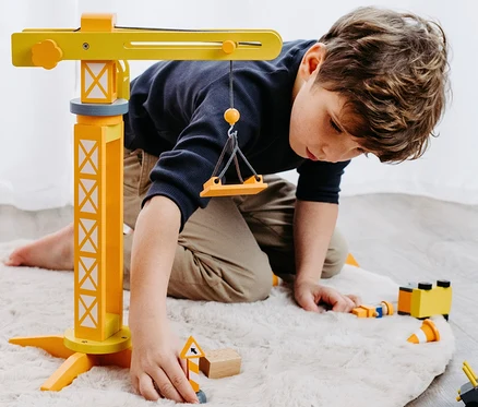 Junge spielt mit einem small foot Baukran mit Baustellenzubehör auf einem beige Teppich.