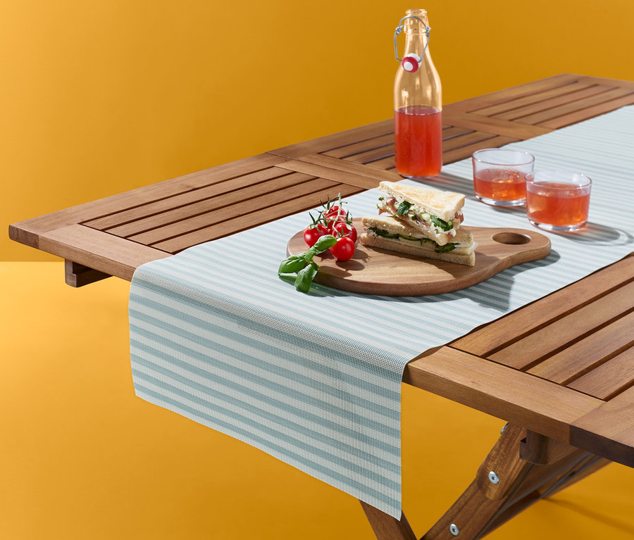 Auf einem Holztisch liegen ein Tischläufer mit Streifen, Speisen und Getränke.