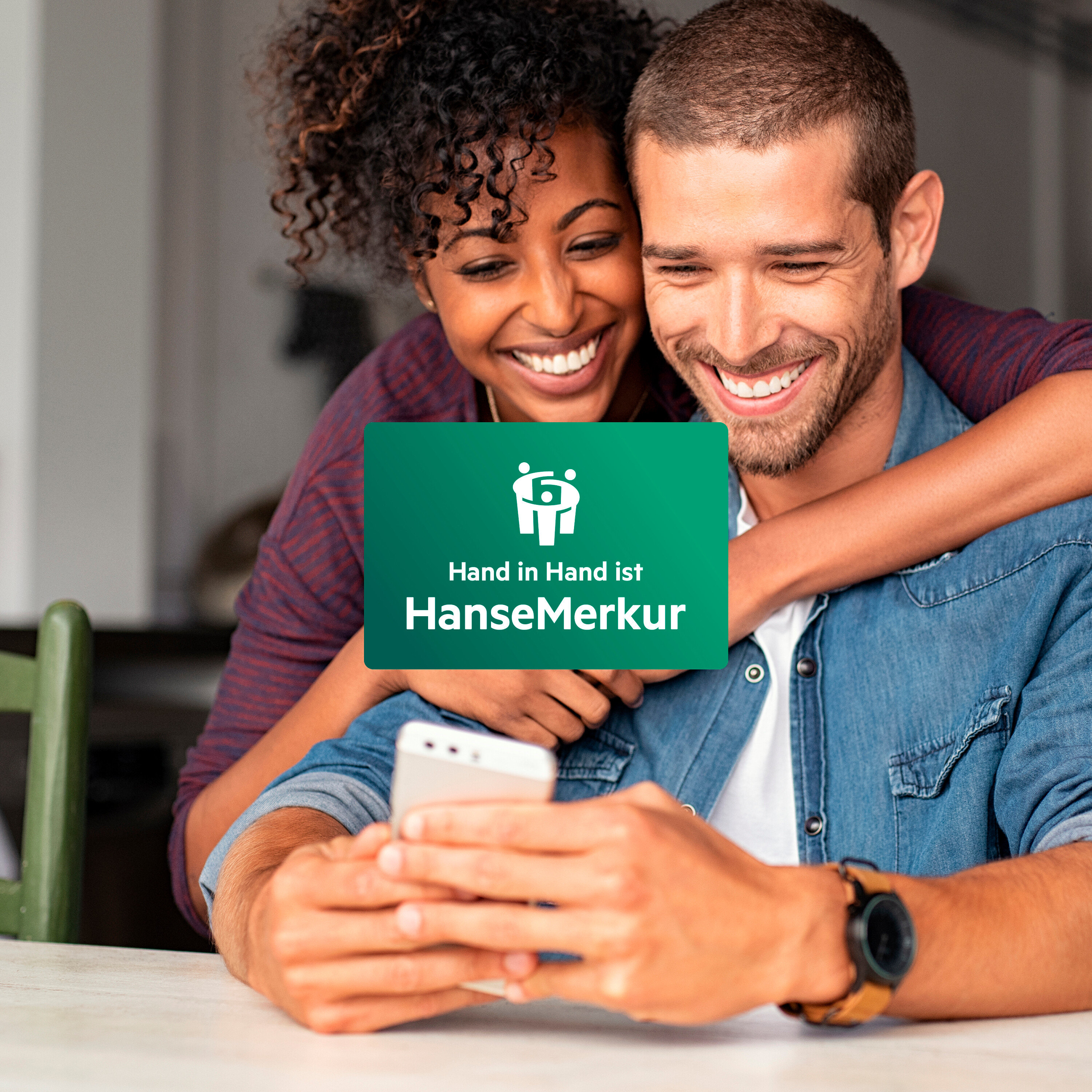 Ein lächelndes Paar schaut auf ein Mobiltelefon, die Frau umarmt den Mann.