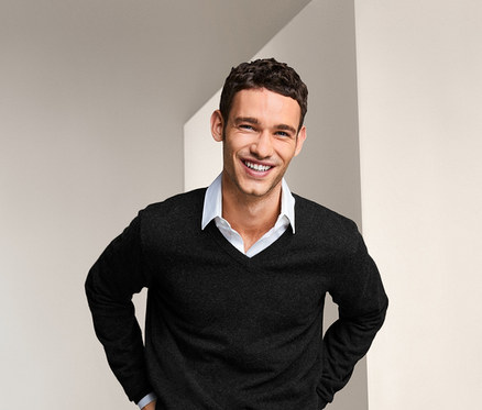 Lächelnder Mann posiert in Cashmere-Pullover mit V-Ausschnitt und Jeans.