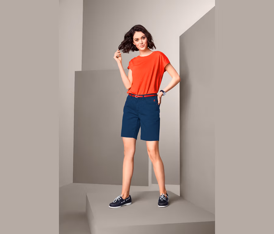 Frau posiert in rotem T-Shirt und Bermudashorts.