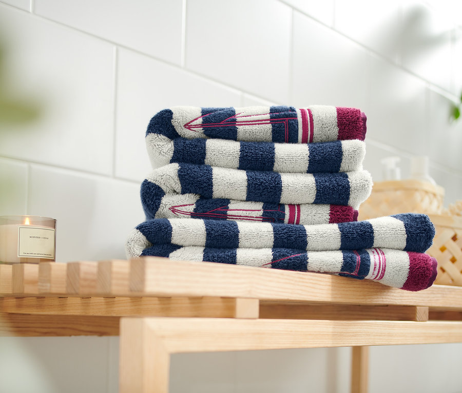 Auf einem Holzregal liegt ein Stapel Handtücher mit blau-weißen Streifen und Stickerei.