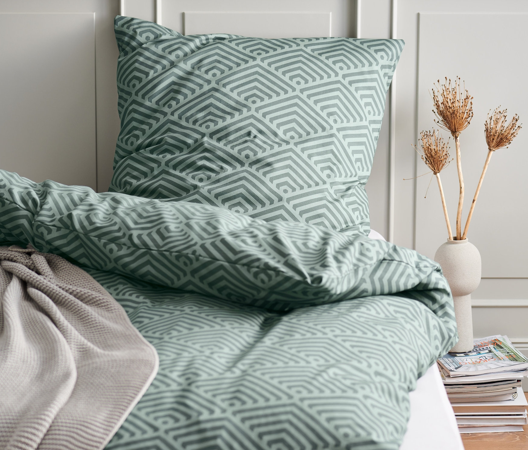 Bettwäsche mit geometrischem Muster auf einem Bett, im Hintergrund eine Wand.