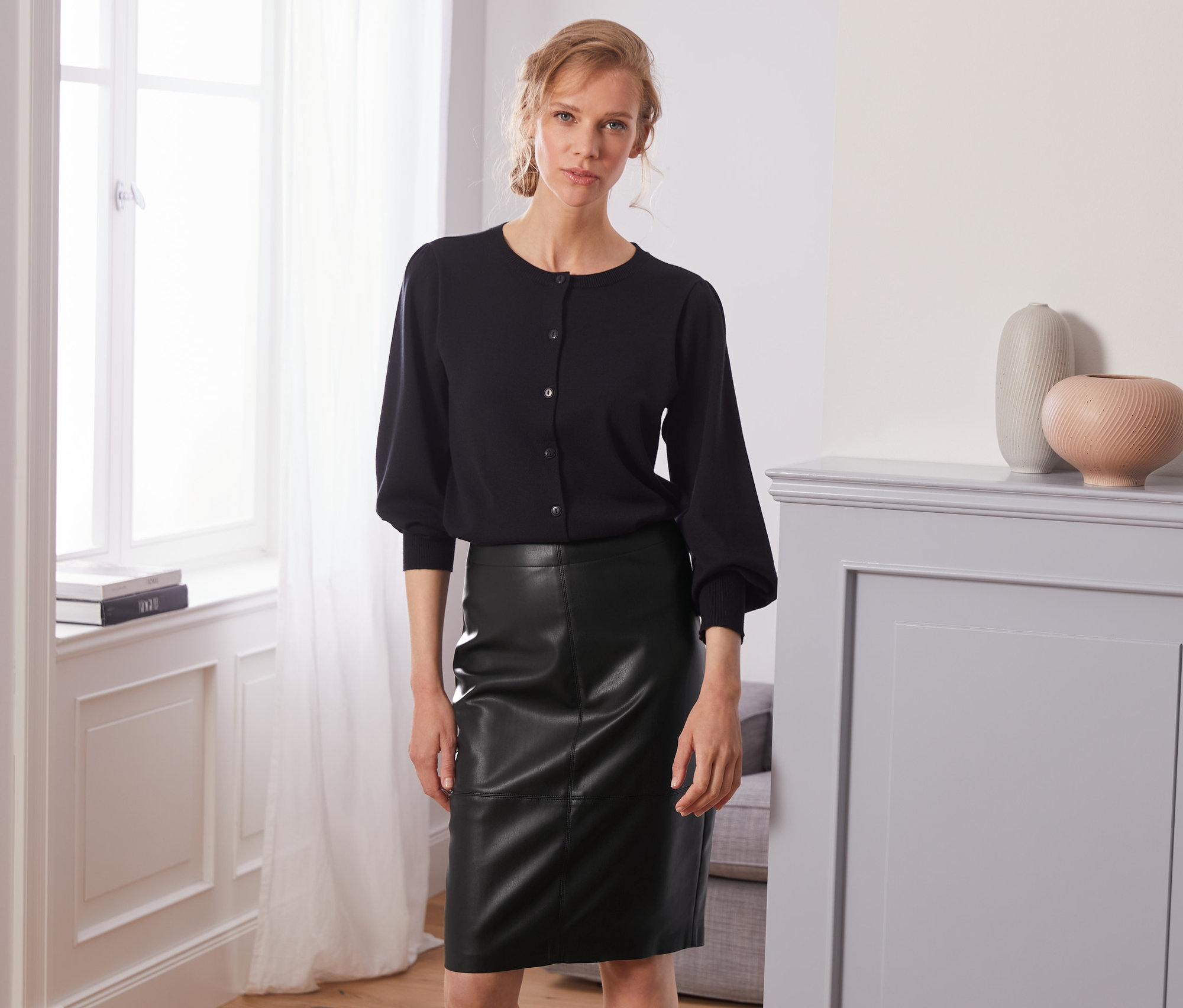 Frau posiert in schwarzem Oberteil und Rock in Lederoptik.