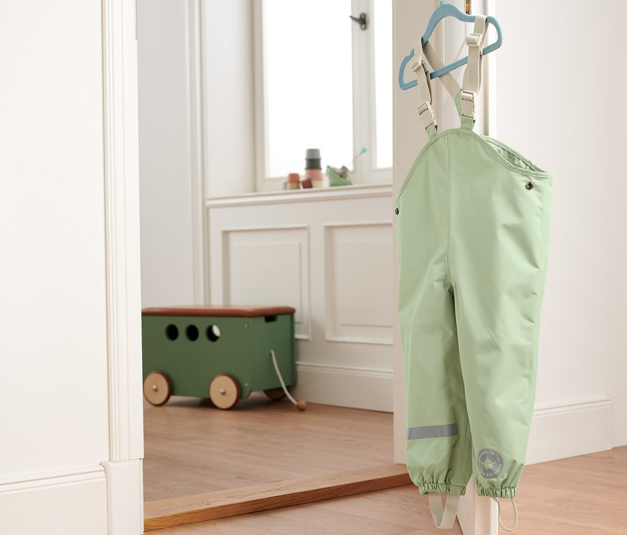 Eine grüne Regenhose hängt an einem Kleiderbügel an einer Tür.