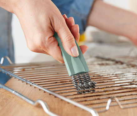 Frau reinigt Backofengitter mit Backofenbürste mit Schaber.