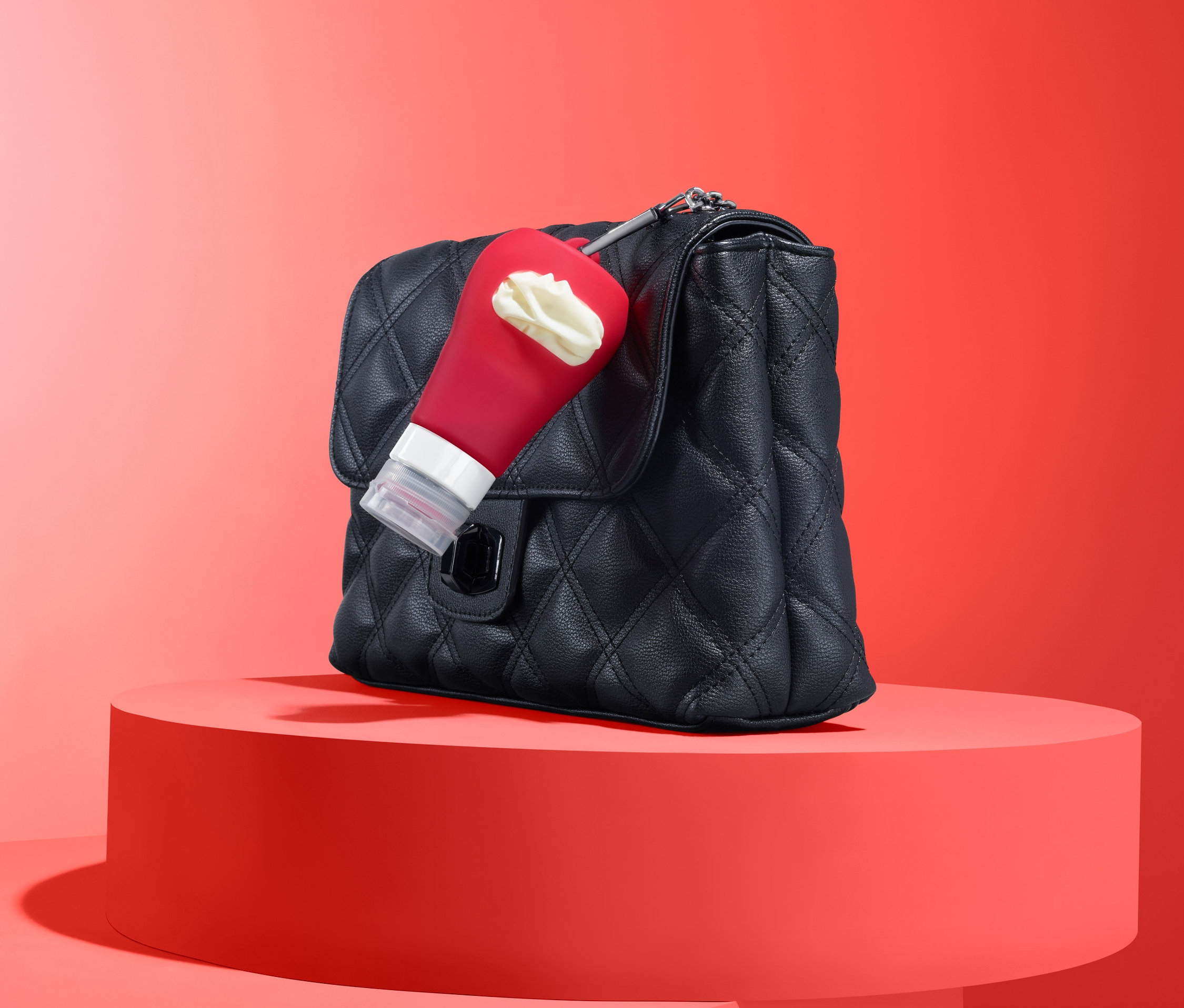 Schwarze Handtasche mit roter Saucenflasche mit weißem Inhalt auf rotem Sockel.