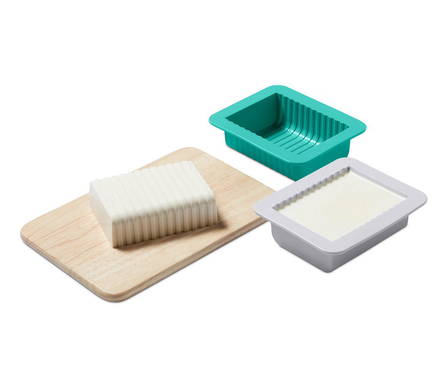 Ein Block Pflanzenbutter auf einem Holzbrett neben einer grünen und einer grauen Form aus dem DIY-Pflanzenbutter-Set.