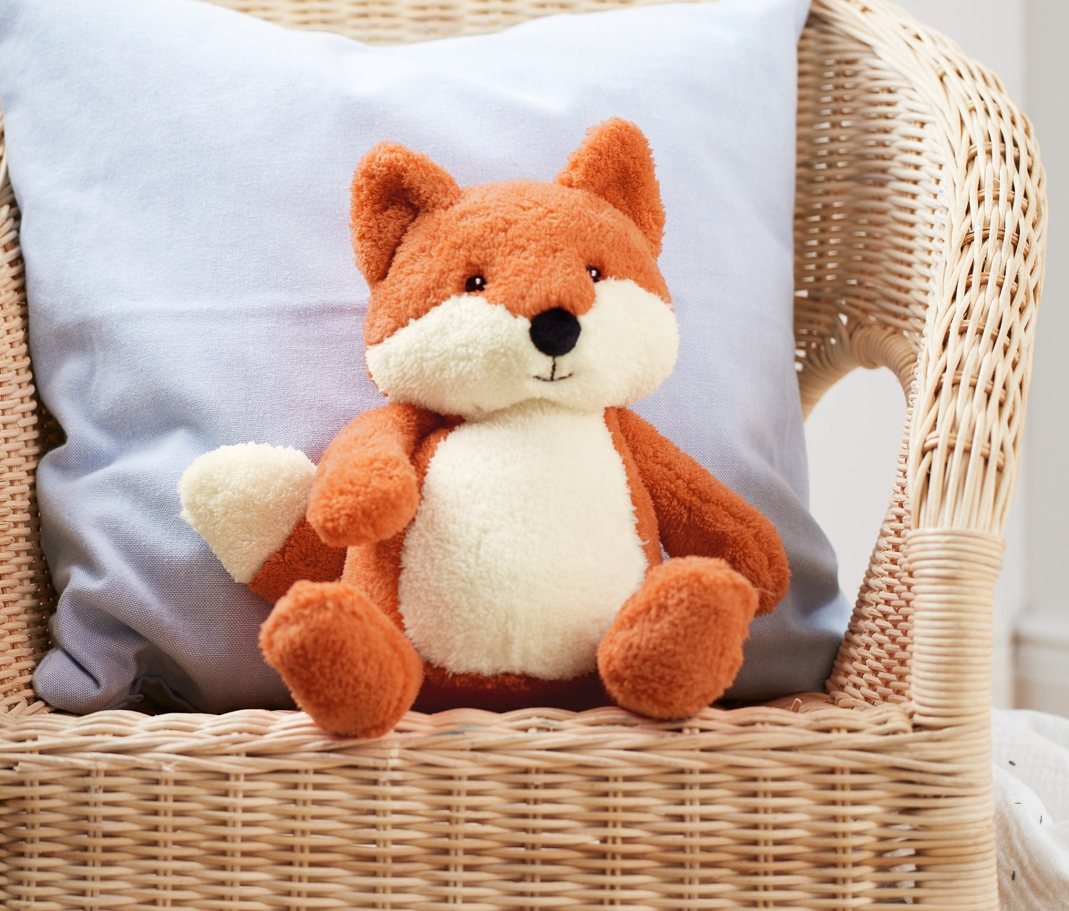 Ein Plüschtier »Fuchs« sitzt auf einem Korbstuhl mit einem blauen Kissen.