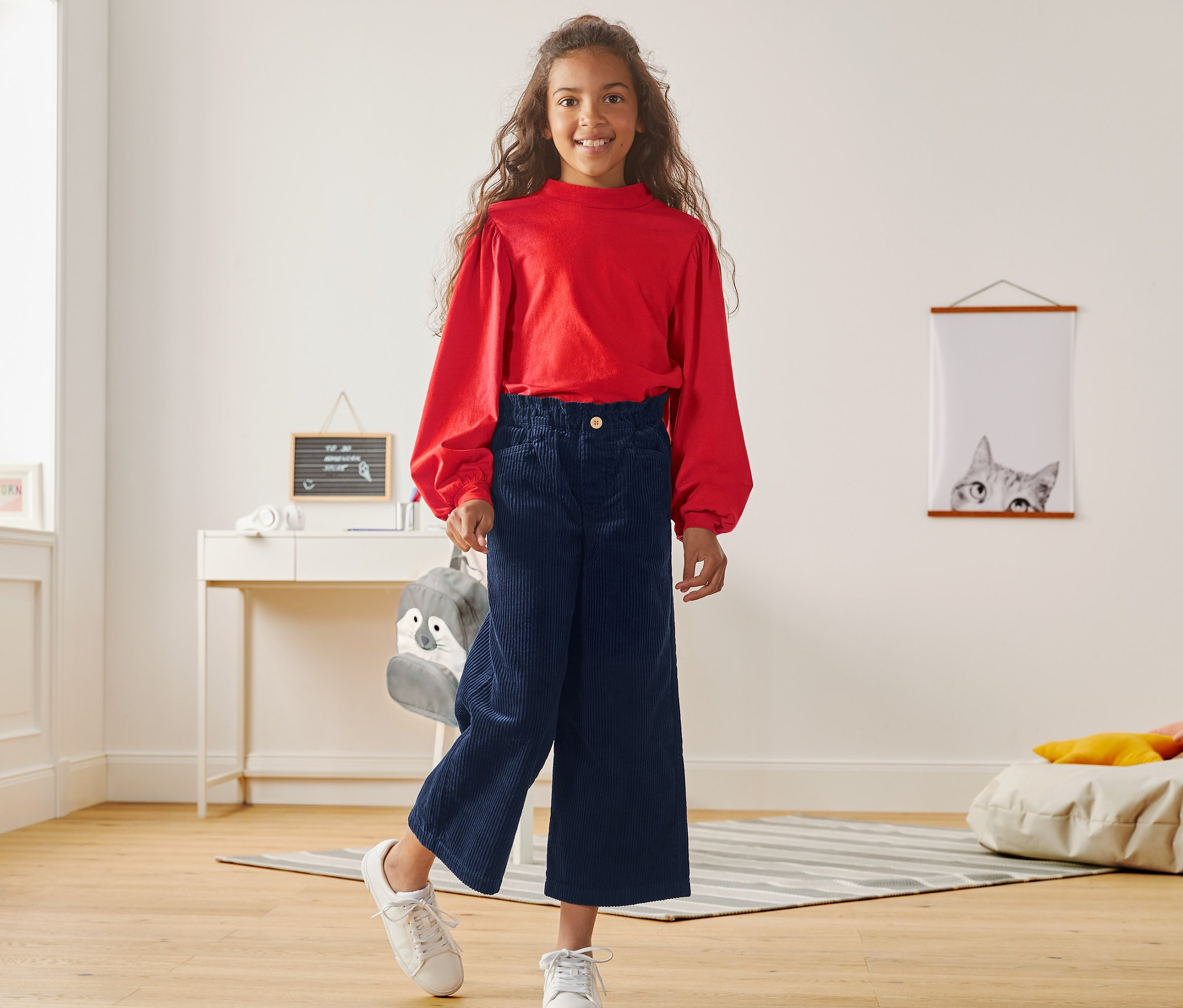 Mädchen posiert in rotem Oberteil und Cord-Culotte.