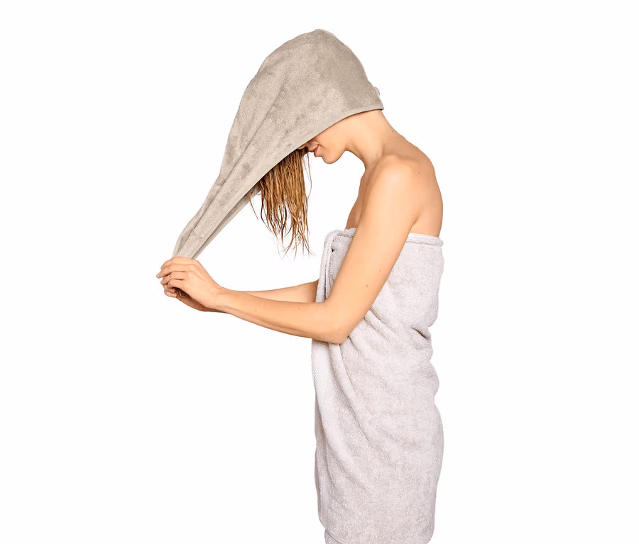 Frau wickelt ein extra saugfähiges Turban-Handtuch in Beige um ihre nassen Haare.
