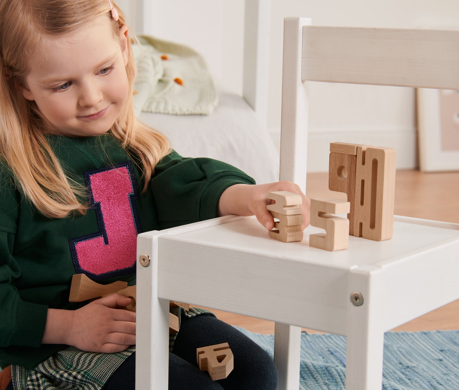 Mädchen spielt mit Zahlenbausteinen auf einem weißen Stuhl.