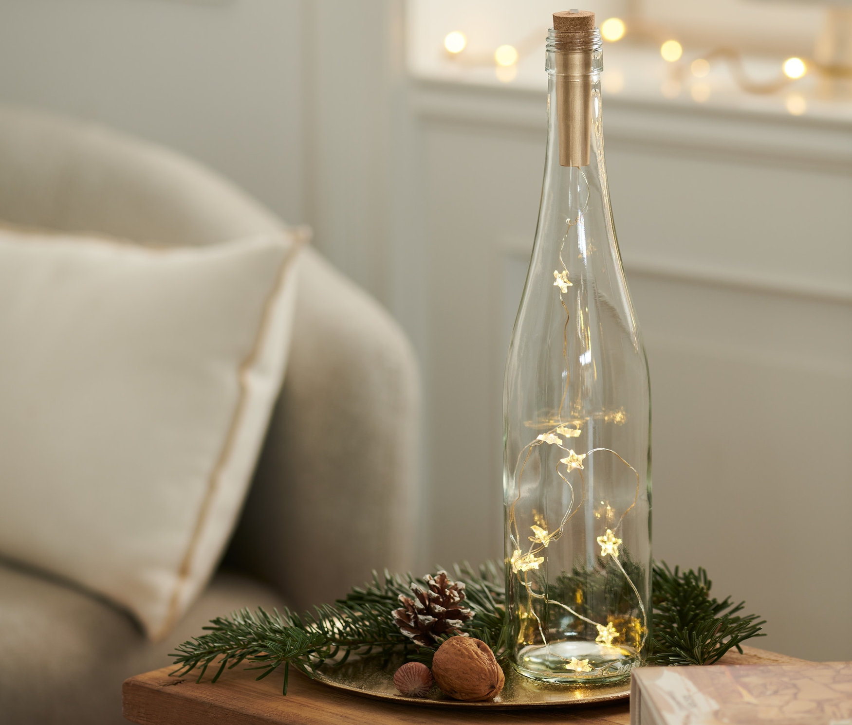 Eine Glasflasche mit LED-Korken steht auf einem Tisch neben einem Buch.