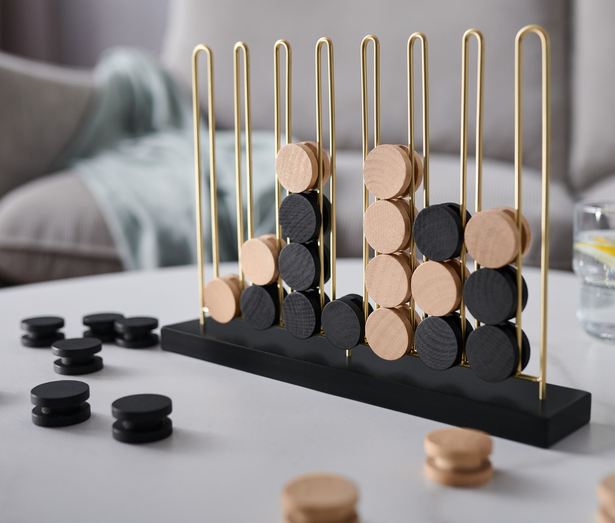 Spiel »4 in einer Reihe« mit schwarzen und hellen Holzscheiben auf einem weißen Tisch.