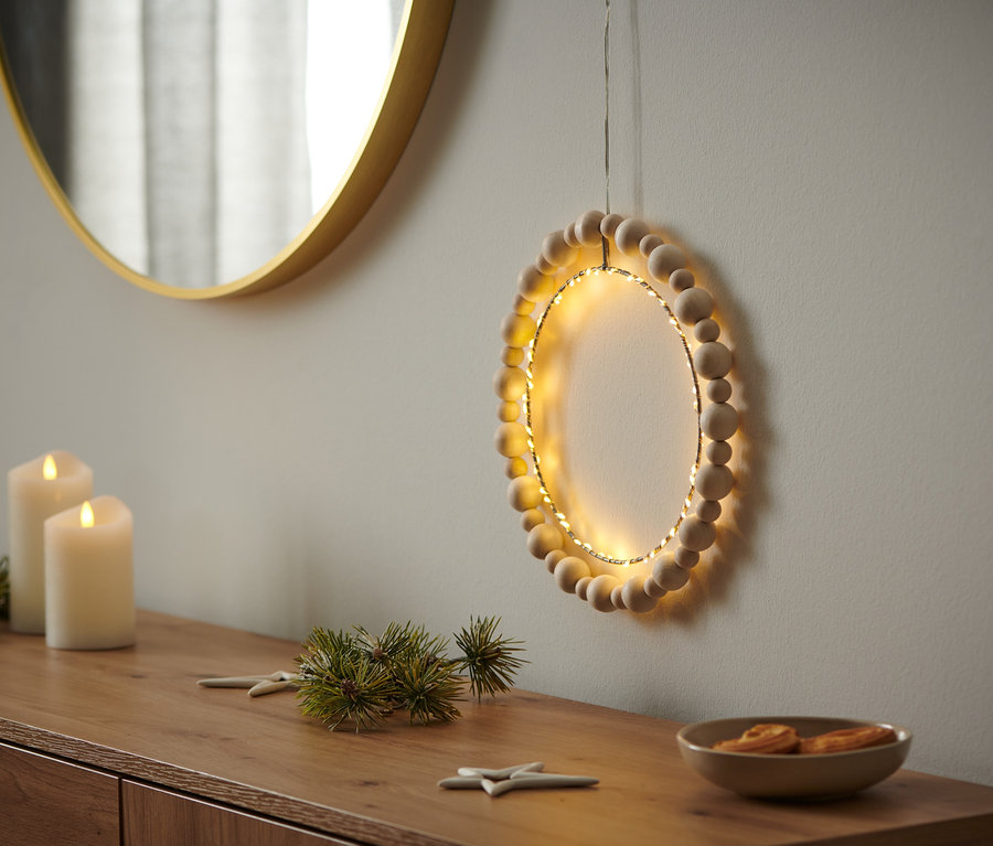 Ein LED-Ring mit Holzperlen hängt an der Wand.