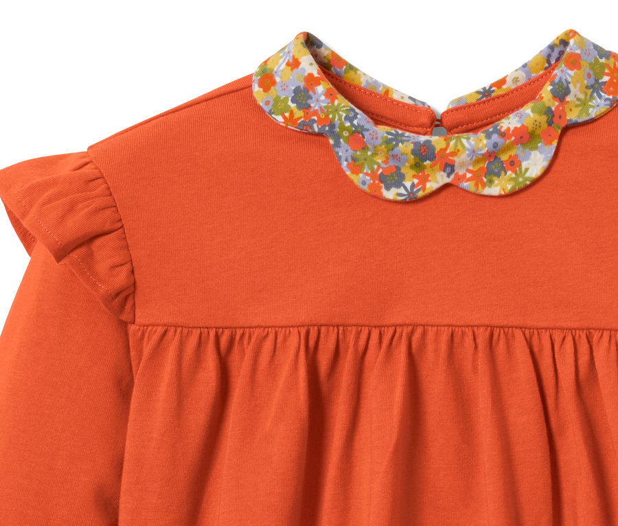 Orangefarbenes Kleinkind-Langarmshirt mit Blumenkragen und Rüschen an den Schultern.