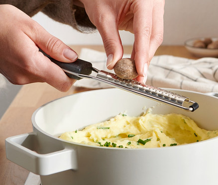 Frau reibt Muskatnuss mit Muskatreibe über einem Topf mit Brei.