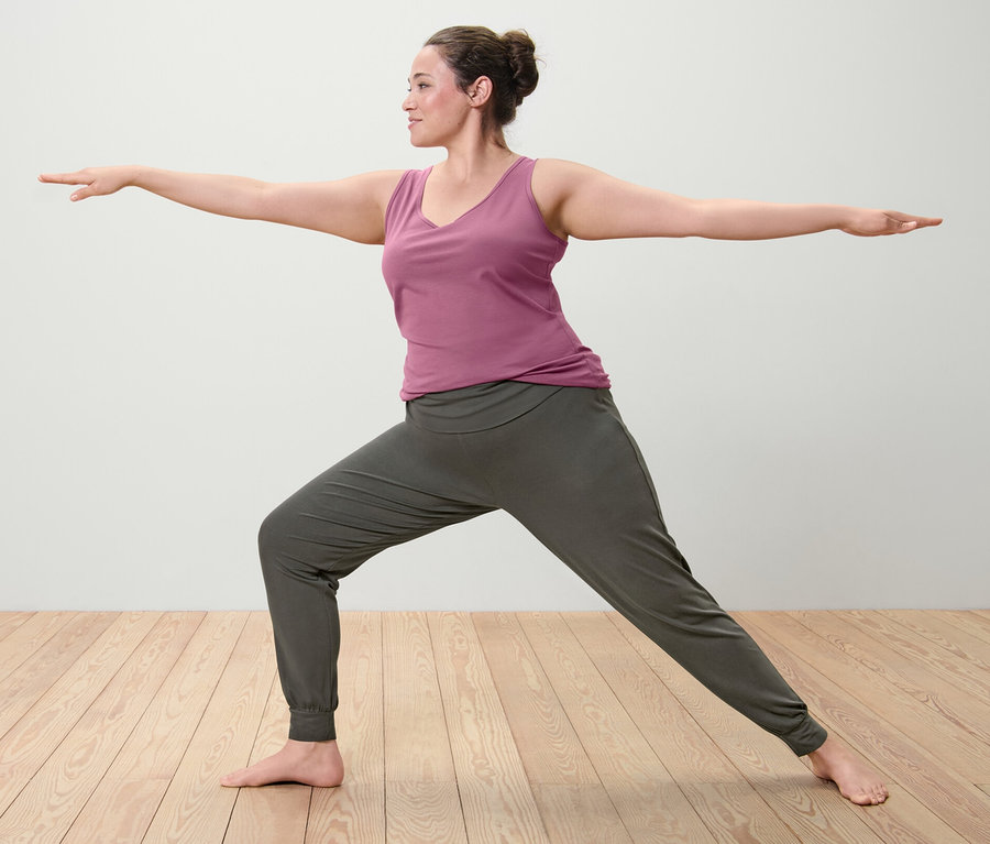 Frau in Kriegerpose mit einem von zwei mauvefarbenen Tops und einer Yogahose.