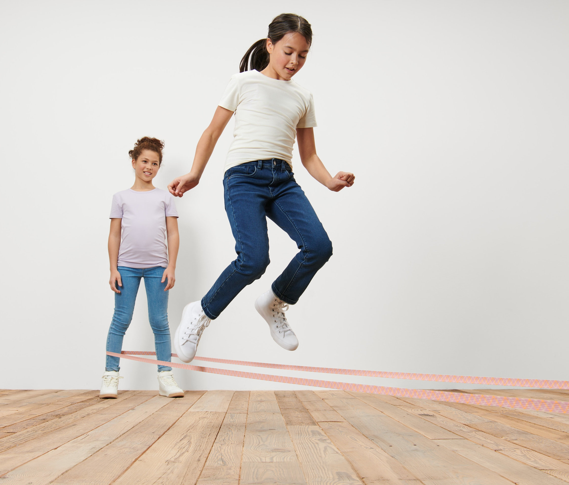 Mädchen springt Gummitwist, anderes Mädchen hält Gummitwist.