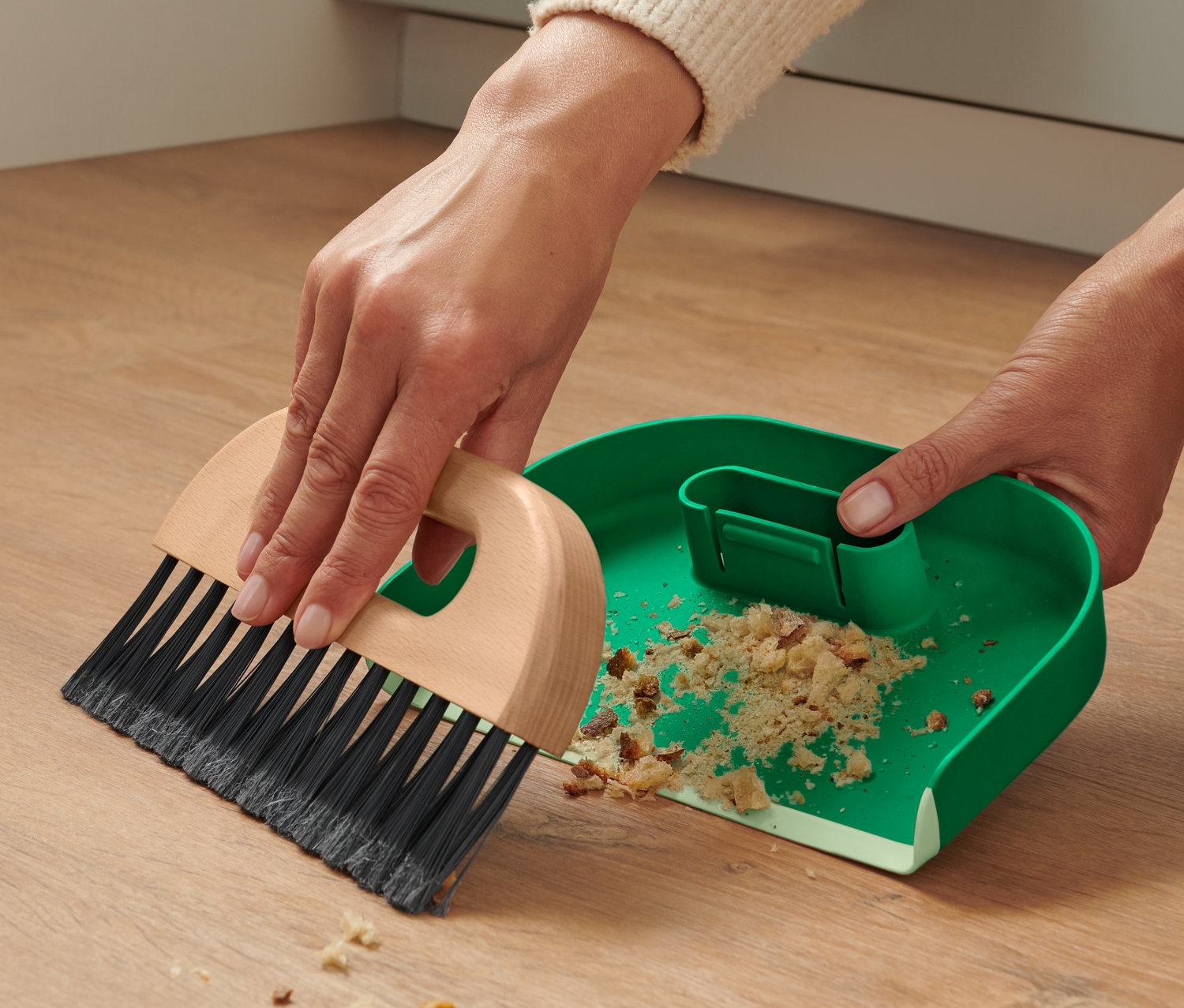 Frau kehrt Krümel mit Handkehrer und Schaufel auf.
