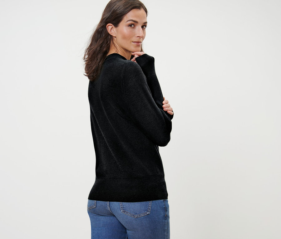 Frau posiert in schwarzem Feinstrickpullover und blauen Jeans.
