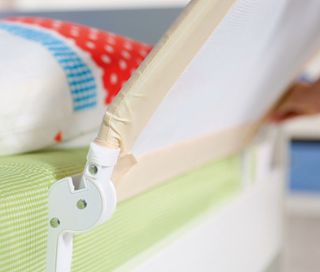 Detail eines beigen roba Bettschutzgitters »Klipp-Klapp«, das an einer Matratze mit einem bunten Kissen befestigt ist.