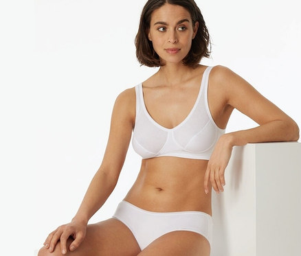 Frau sitzt und trägt ein weißes 2 SCHIESSER Bustiers mit Cups und Bio-Baumwolle.