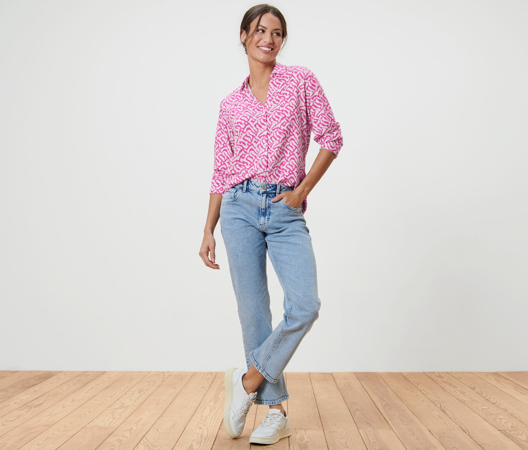 Frau steht mit der Hand in der Tasche und trägt ein Blusenshirt mit Knopfleiste.