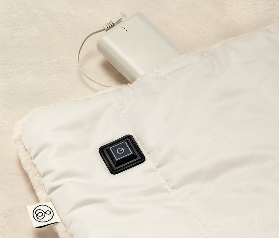 Detailansicht eines Akku-Heizponchos mit Bedienknopf und angeschlossenem Akku.