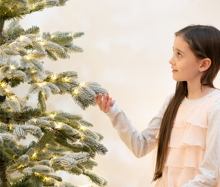 Mädchen betrachtet eine beschneite Evergreen LED-Tanne »Nobilis«, 150 cm hoch.