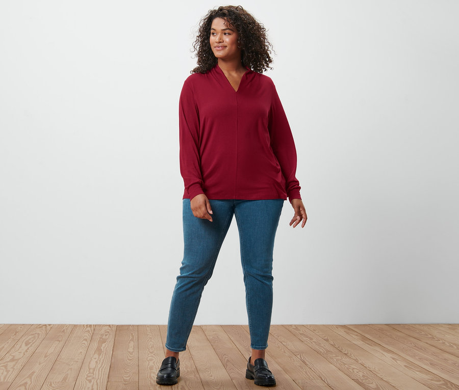 Frau steht in bordeauxrotem Langarmshirt mit V-Ausschnitt, Treggings »Fit Nelly« und Leder-Loafern.