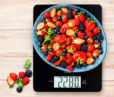 Auf der schwarzen ADE Digitale Küchenwaage Leonie steht eine blaue Schale voller Erdbeeren, Himbeeren, Blaubeeren und Brombeeren.