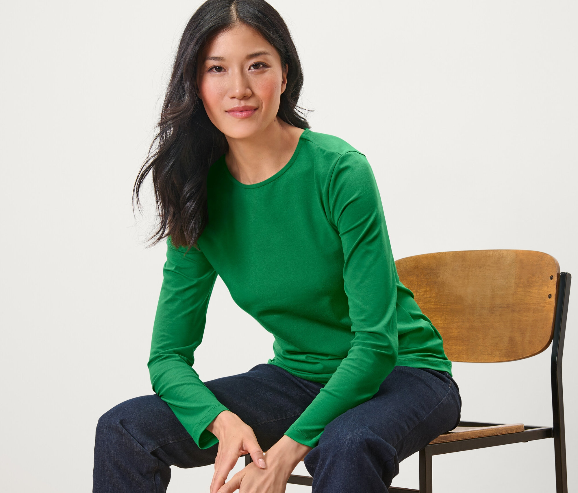 Frau sitzt auf einem Stuhl und trägt ein grünes Langarmshirt.