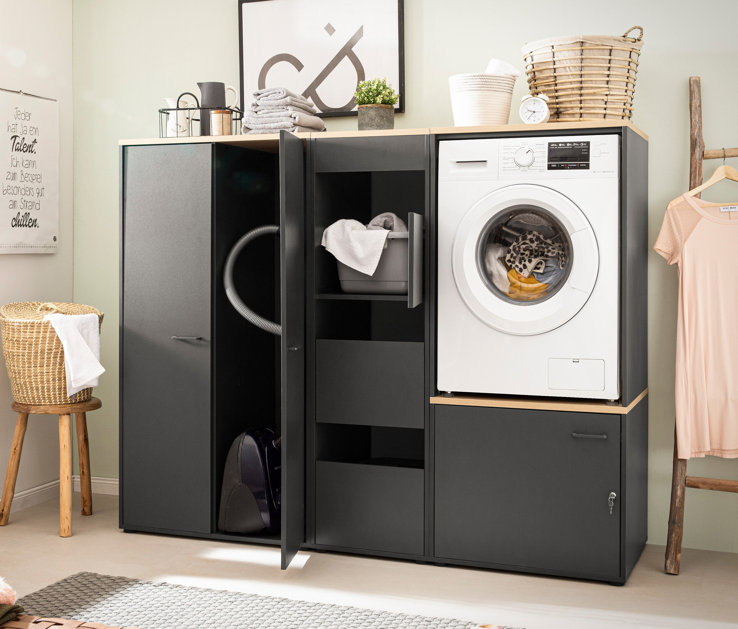 Ein Badezimmer zeigt einen Waschmaschinenumbau »Solea« inkl. Unterschrank, anthrazit, daneben einen Mehrzweckschrank »Solea«, anthrazit, und einen offenen Unterschrank »Solea«, abschließbar, anthrazit.
