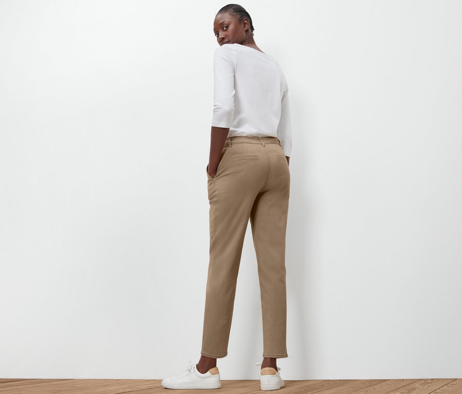 Frau posiert mit dem Rücken zur Kamera in beigen Chinos.