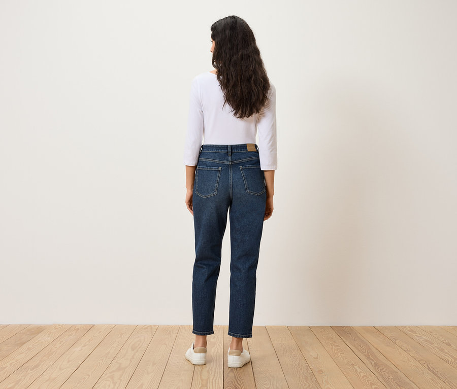 Rückansicht einer Frau mit dunklen Haaren in blauen Jeans, weißem T-Shirt und weißen Schuhen.