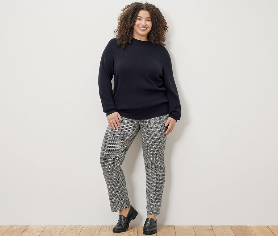 Lächelnde Frau posiert in dunkelblauem Feinstrickpullover und bedruckter Stretchhose.