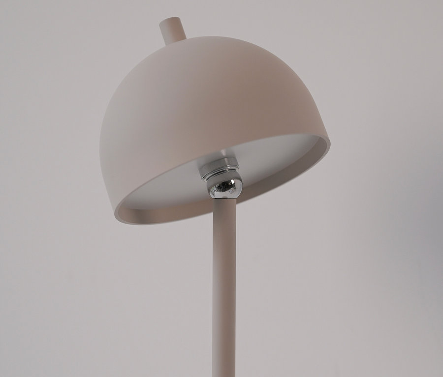 Detailaufnahme einer beigen Lampe mit rundem Schirm und silberner Glühbirne.