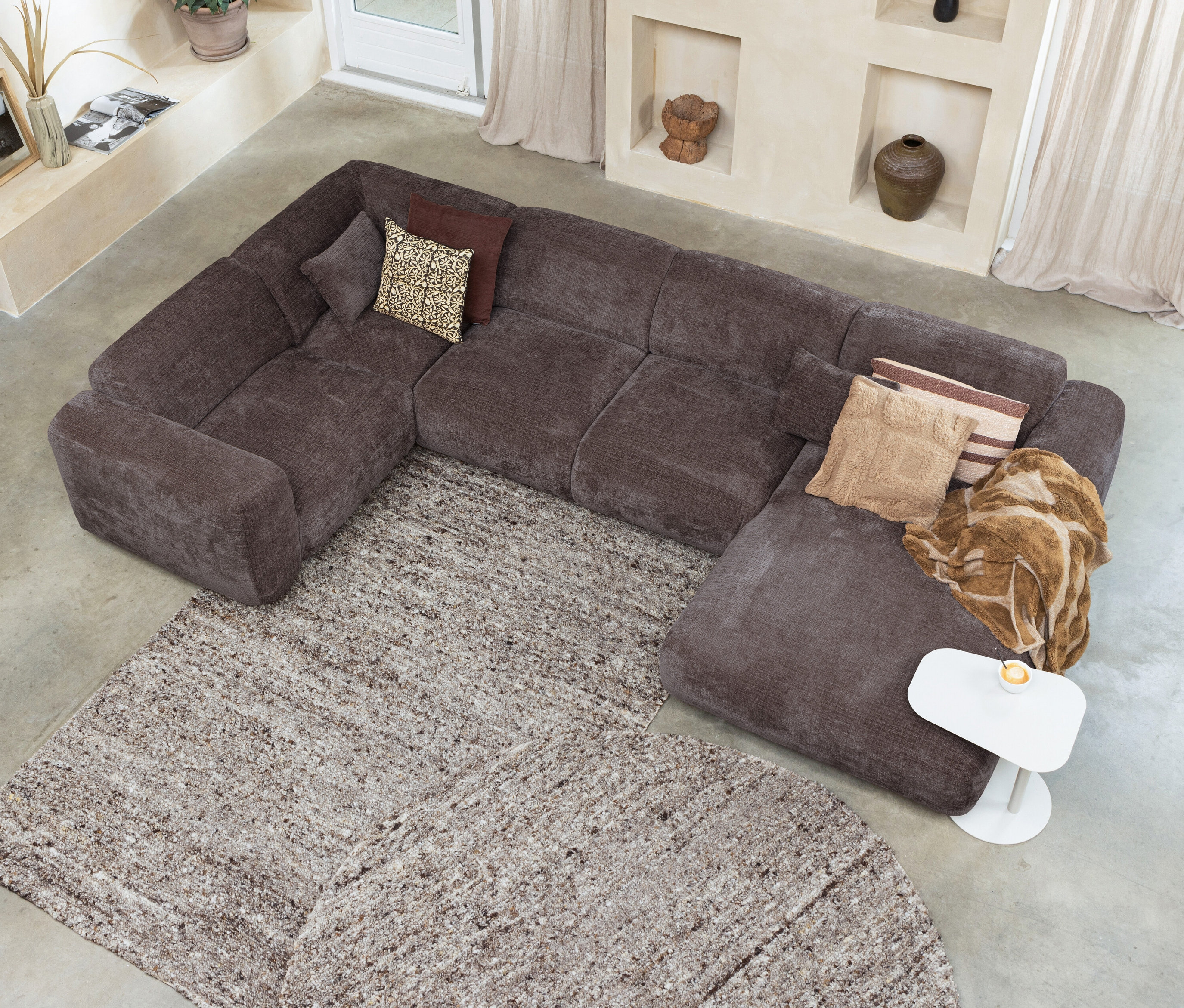 Draufsicht auf ein braunes Ecksofa mit Kissen auf dem beige Teppich Woood Efia, 170 x 240 cm.