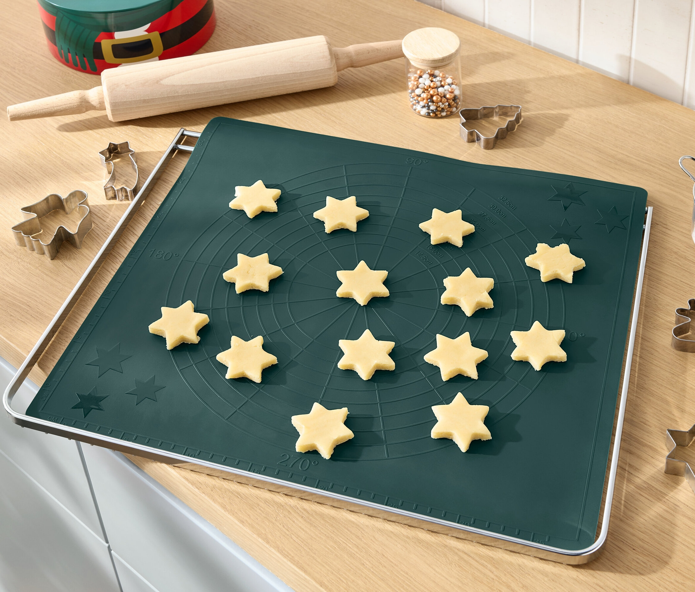 Teigsterne auf grüner Backmatte mit Nudelholz, Streuseln und Ausstechformen.