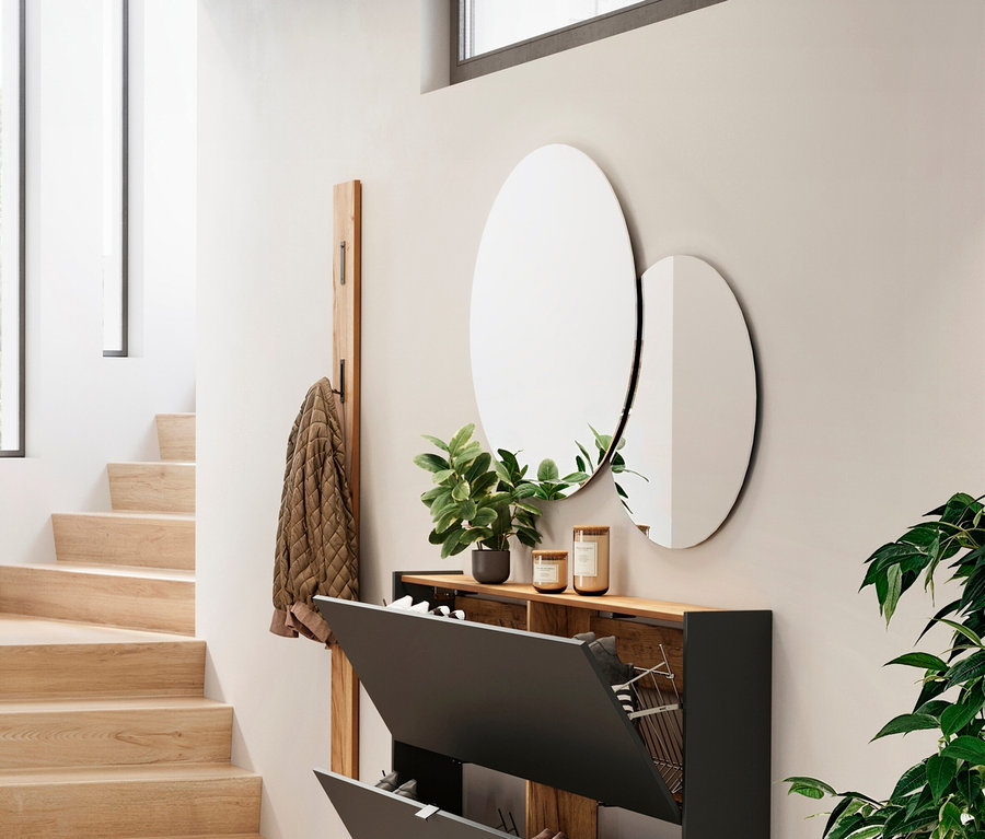 Eingangsbereich mit Schuhschrank, zwei runden Spiegeln, Topfpflanzen und Garderobe mit Jacke.