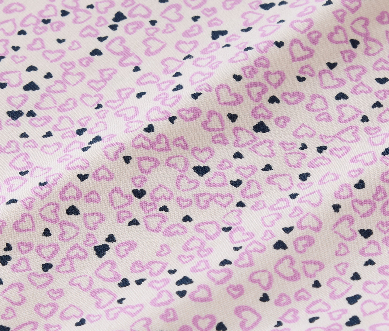 Detailaufnahme eines Stoffes, der mit kleinen rosa und dunkelblauen Herzen auf weißem Hintergrund bedruckt ist.