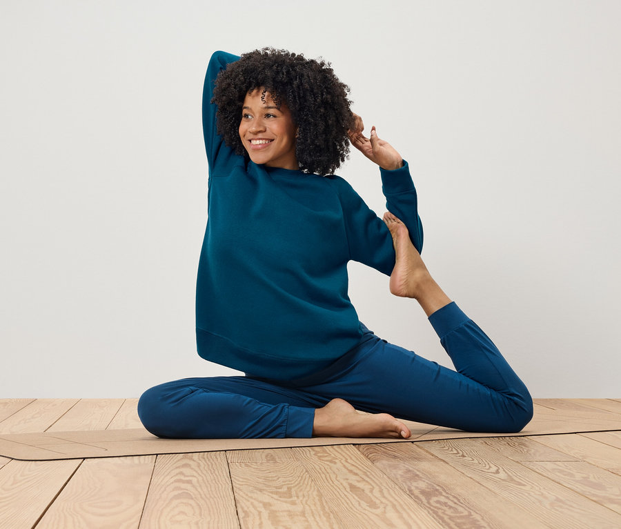 Afroamerikanische Frau in blauem Trainingsanzug macht Yoga auf einer Matte.