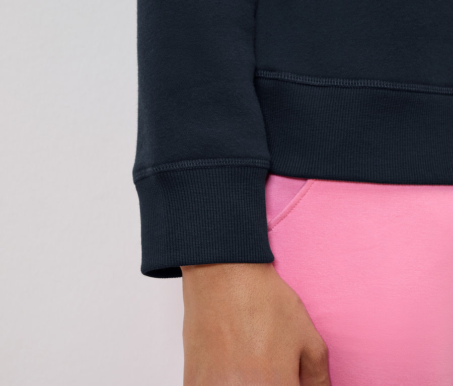Detailaufnahme eines dunkelblauen Sweatshirt-Ärmels und eines Teils einer pinkfarbenen Hose.
