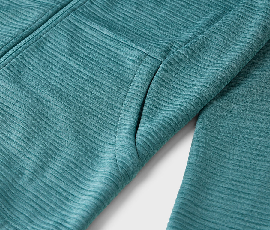 Nahaufnahme einer petrolfarbenen Textiljacke mit Reißverschluss und Tasche.