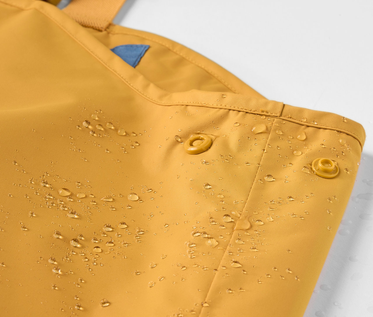 Detailaufnahme einer Kinder-Regenhose mit Wassertropfen.