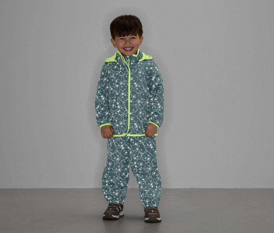 Ein Junge in einer grauen Bärenmusterjacke und -hose mit neongelben Akzenten lächelt.